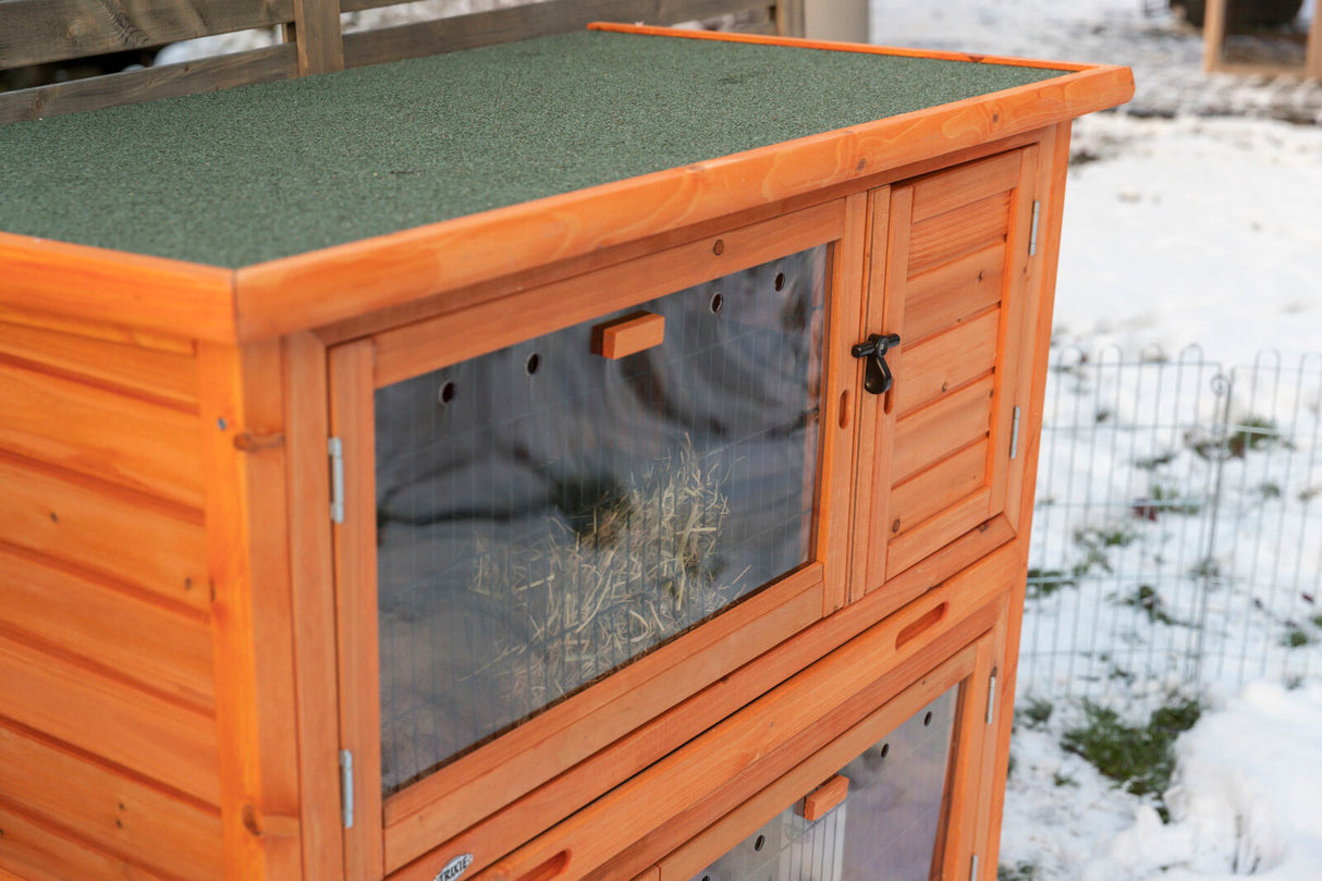 Holzstall mit grünem Dach, transparenten Klappen und schwarzem Verschluss, steht im schneebedeckten Außenbereich.