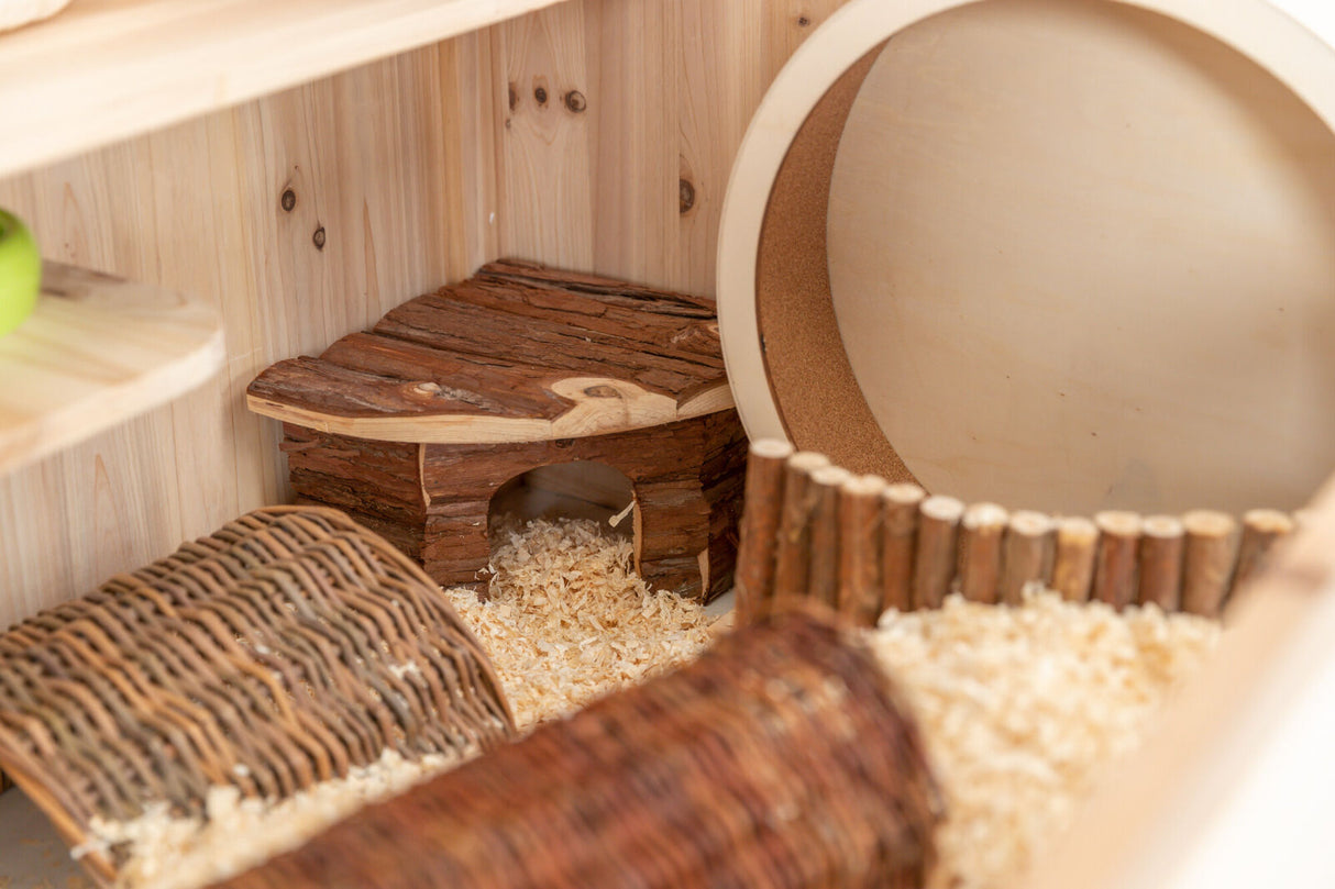 Holzgehäuse mit Rindenhaus, kleinem Laufstall und Holzspänen auf dem Boden, daneben eine runde Öffnung.
