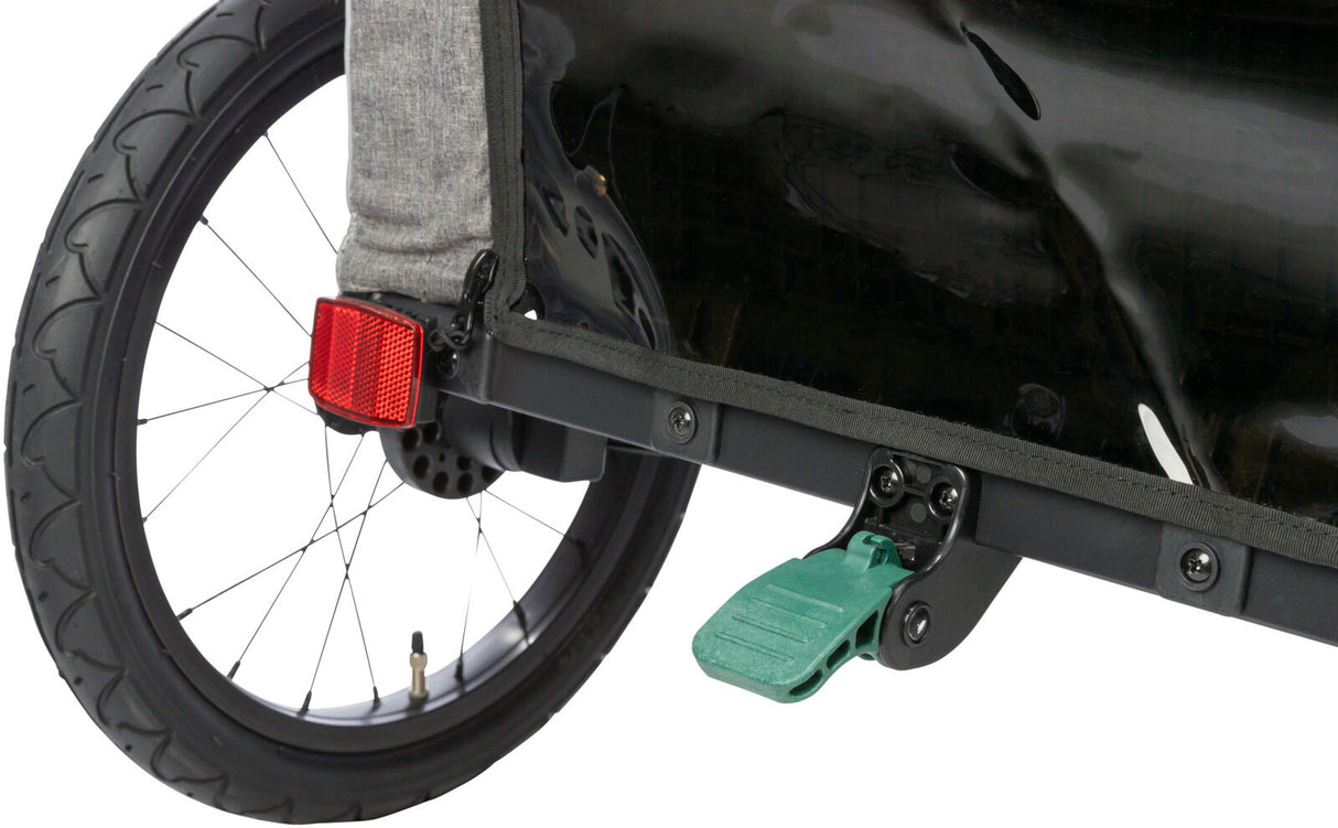 Rad eines Fahrradanhängers mit rotem Reflektor, schwarzem Schutzblech und grünem Pedal auf grauer Stoffbespannung.