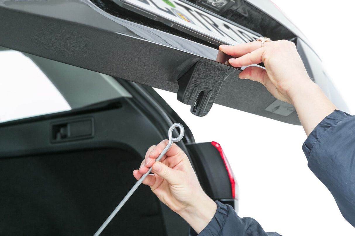 Eine Person hält eine Metallstange mit Öse, die an einem Haken unterhalb einer Autotür eingehängt wird.