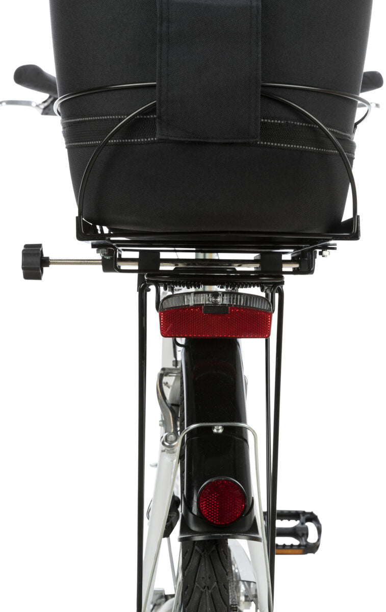 Fahrradträger mit schwarzem Behälter über dem Hinterrad und rotem Reflektor darunter, teilweise sichtbare Pedale.