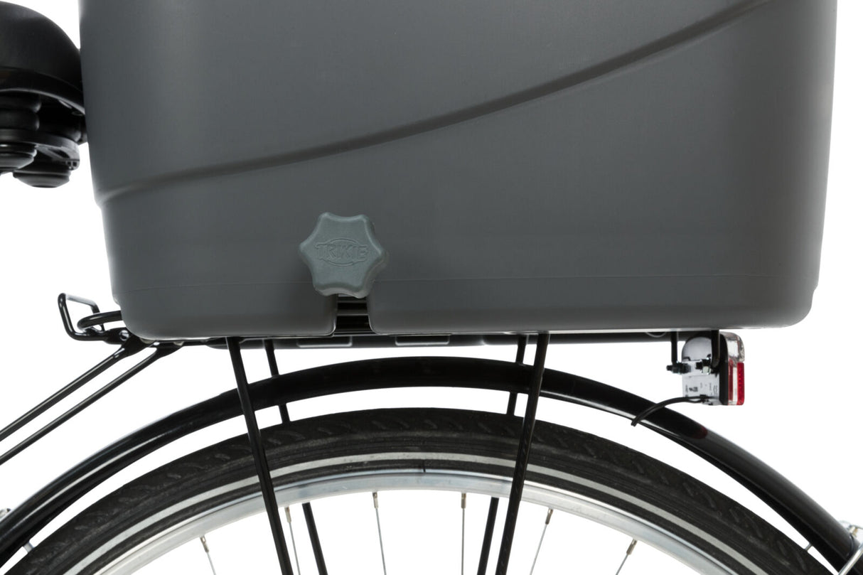 Grauer Fahrradanhänger mit Verschluss über einem schwarzen Fahrradreifen montiert, Herstellername auf Verschluss sichtbar.