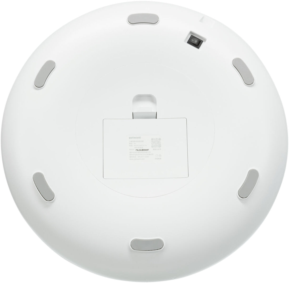 Rundes weißes Gerät mit grauen Standfüßen und zentralem Fach, Text und ein Schalter sind sichtbar.