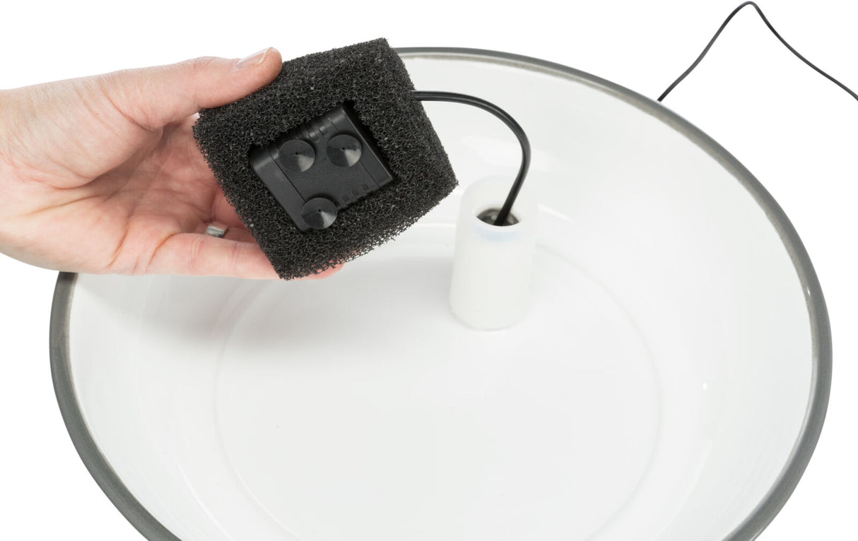 Eine Hand hält einen schwarzen Schaumstoffblock mit integriertem Kabel über einer weißen, runden Schale.
