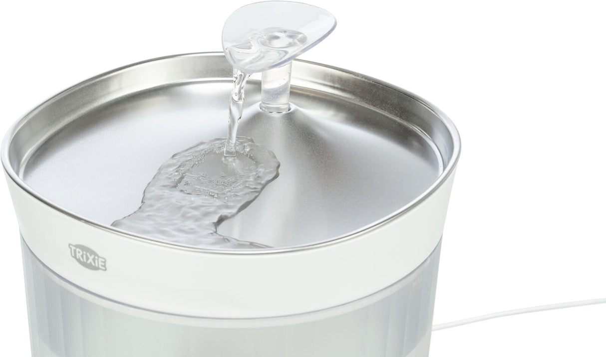 Ein weißer Trinkbrunnen mit fließendem Wasser über einer metallisch glänzenden Oberfläche.