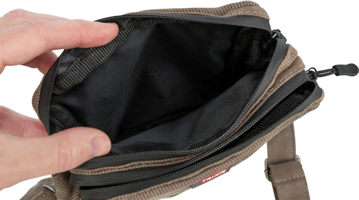 Die geöffnete braune Tasche mit schwarzem Innenfutter zeigt einen Reißverschluss und wird von einer Hand gehalten.