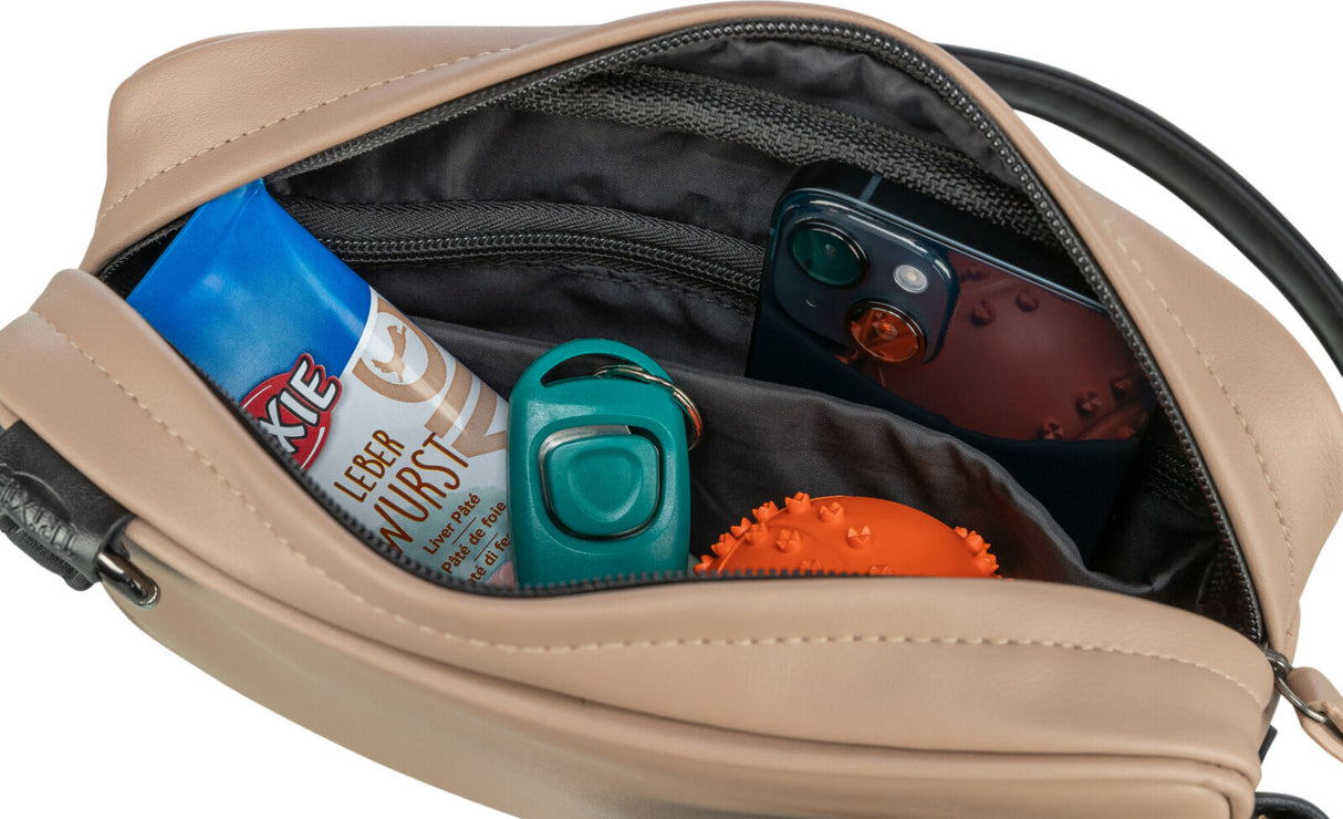 Geöffnete beiger Lederhandtasche mit Handy, blaue Wurstverpackung, orange Noppenball und türkisfarbenem Klicker.