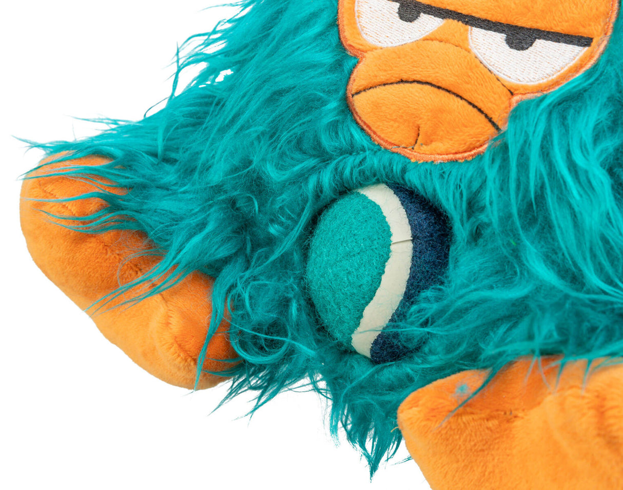 Plüschspielzeug mit orangefarbenem Gesicht, ausdrucksstarken Augen und grüner, zottiger Oberfläche hält einen zweifarbigen Ball.