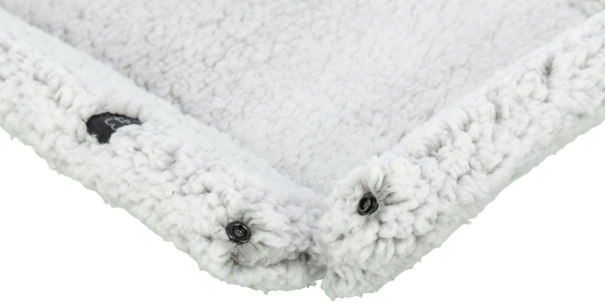Eine weiße, flauschige Decke mit einer dichten Textur, schwarzen Knöpfen und einem kleinen, schwarzen Etikett.