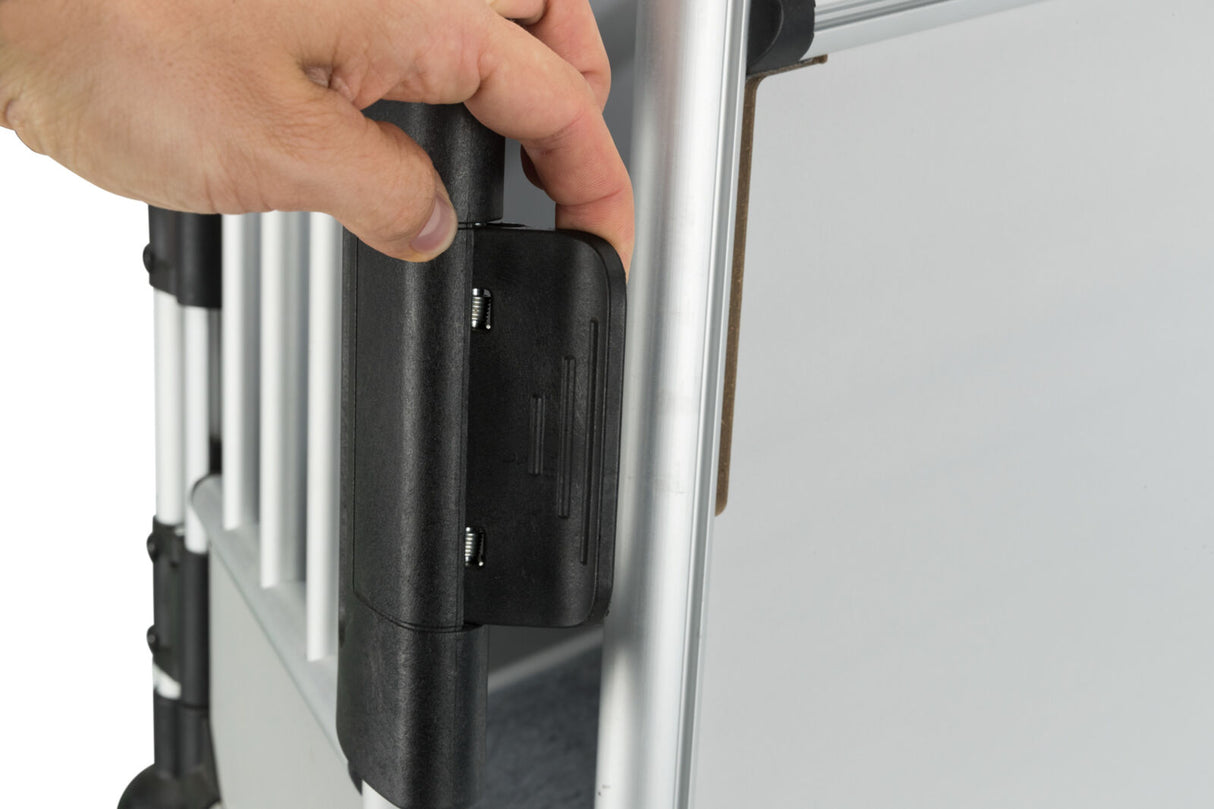 Ein Finger drückt auf eine schwarze Verriegelung an einem silbernen Metallrahmen mit vertikalen Stäben.