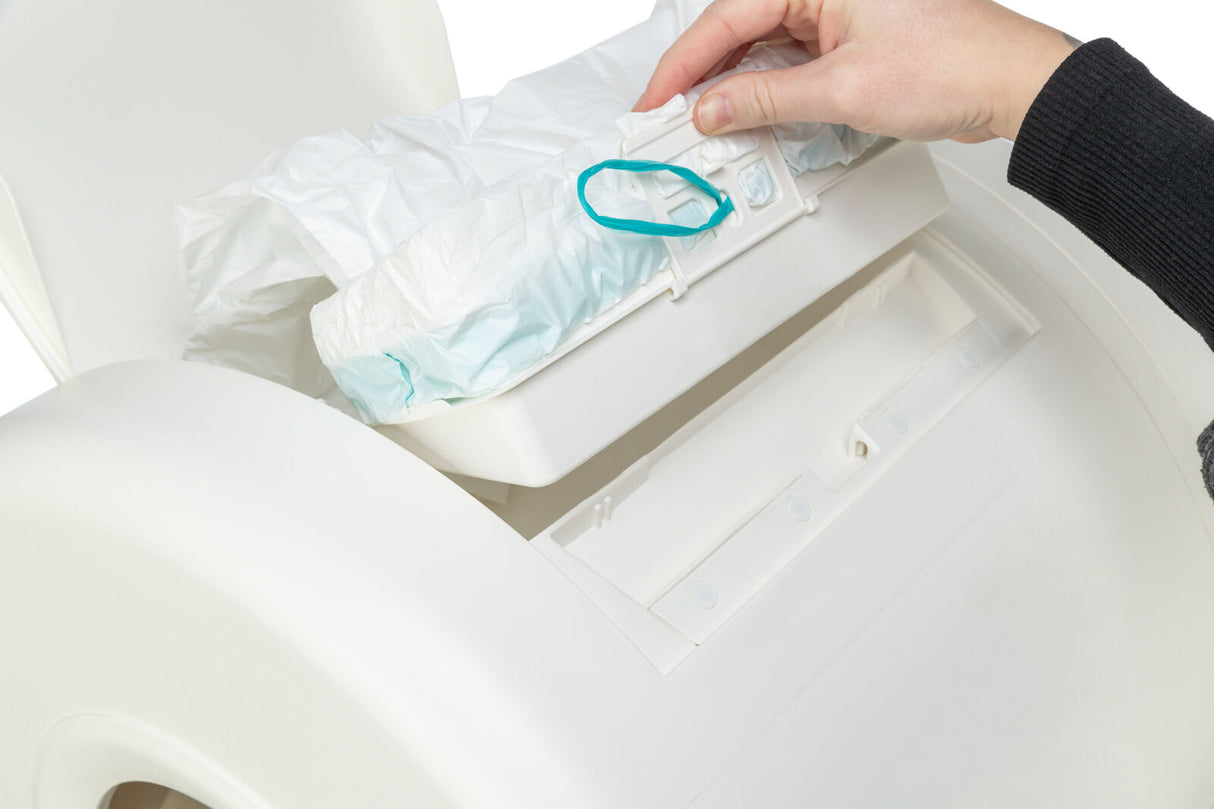 Eine Hand befestigt einen Plastikbeutel mit einer grünen Schlaufe in einem weißen Mülleimer.