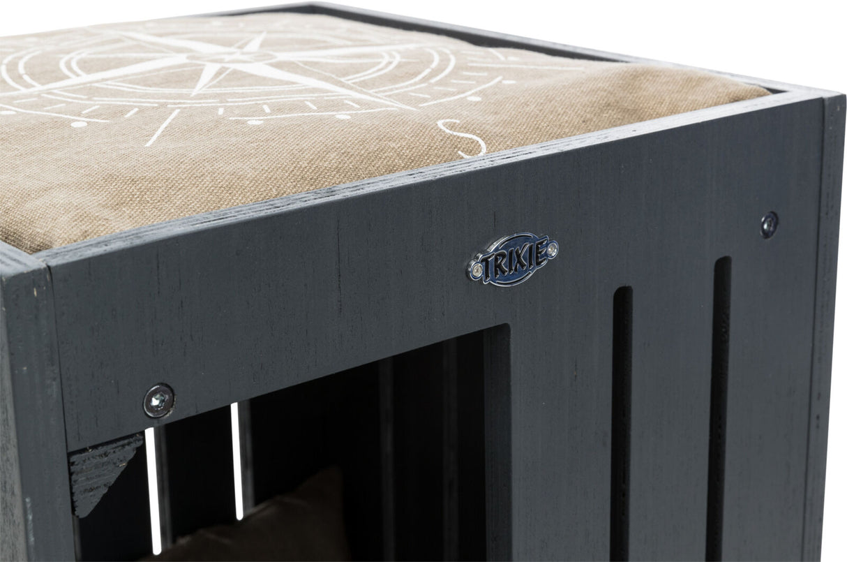 Graue Holzkiste mit beigem Kissen und Kompassmuster, darauf ein Trixie-Label, sichtbare Schrauben.