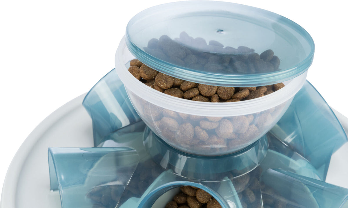 Transparenter Futterspender mit blauem Deckel, gefüllt mit braunen Trockenfutter-Pellets auf weißem Untergrund.