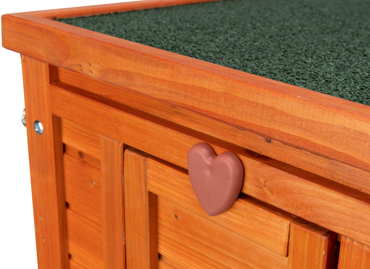 Holzstruktur mit Herzgriff und grünem Dach, Holz ist orange, Griff aus Plastik, Oberfläche körnig strukturiert.
