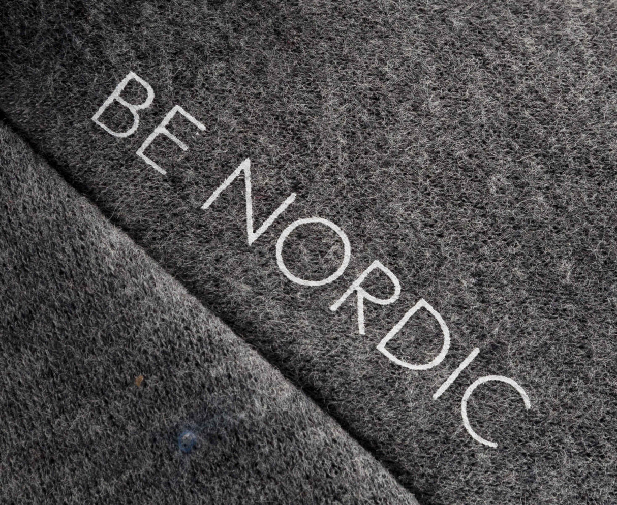 Grauer Textilstoff mit der Aufschrift "BE NORDIC" in weißen Buchstaben.
