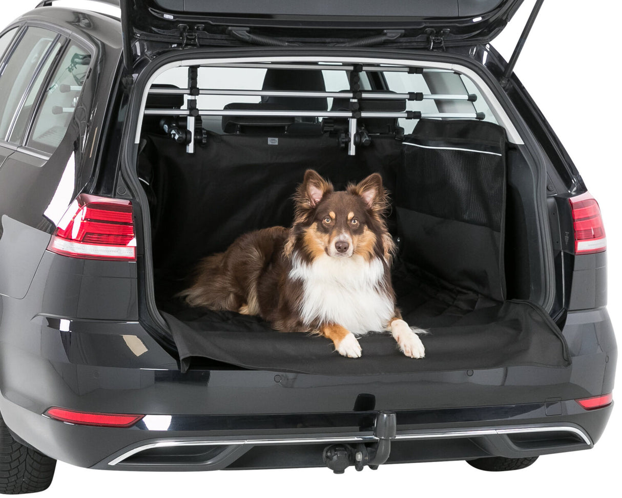 Ein Hund liegt auf einer schwarzen Schutzmatte im geöffneten Kofferraum eines grauen Autos.
