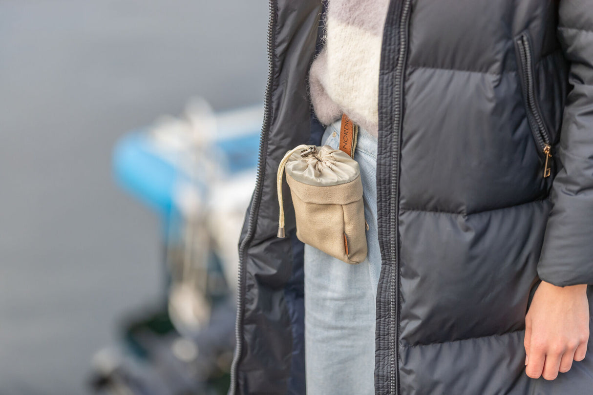 Person in blauer Steppjacke mit beiger Stofftasche und Kordelzug an der Hüfte, unscharfer Hintergrund.