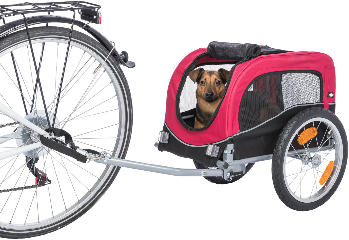 Roter Fahrradanhänger mit einem Hund sitzt darin, Anhänger ist an einem Fahrrad befestigt, seitliche Rollen und Netzfenster.