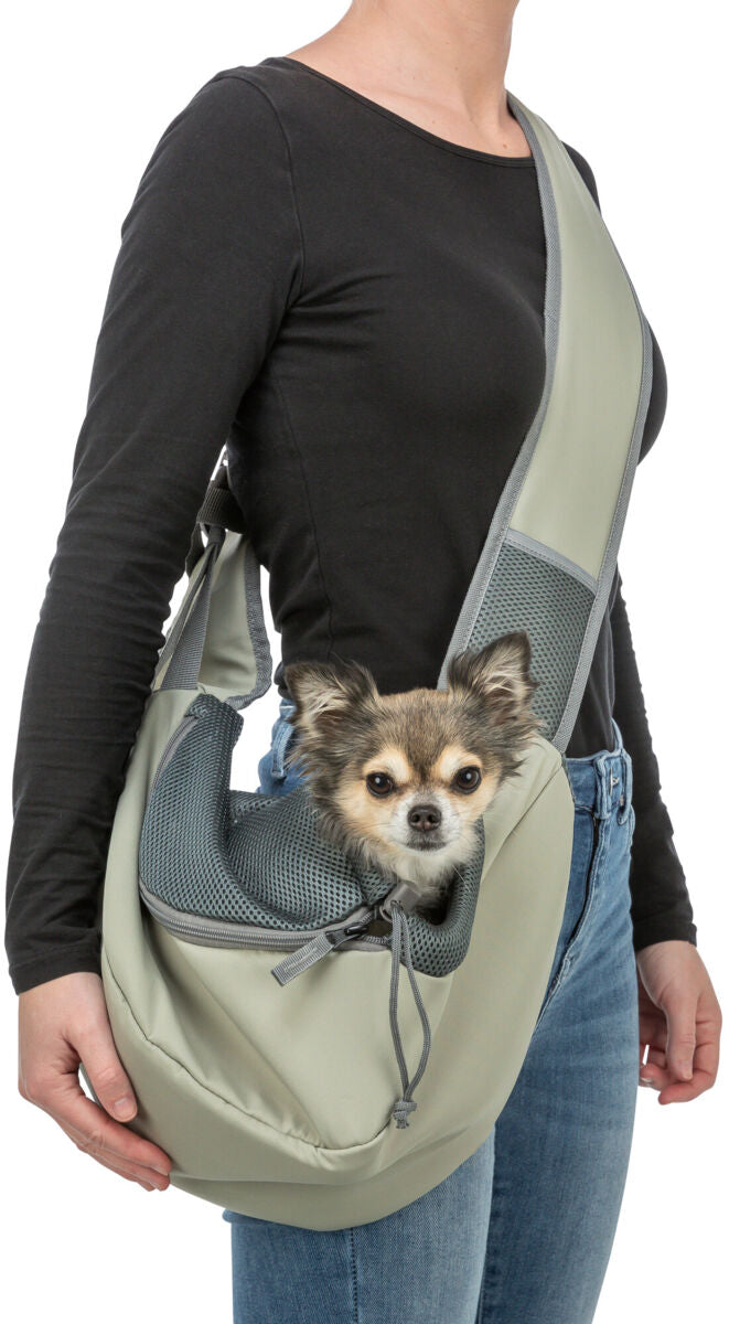 Person trägt eine beigefarbene, crossbody Hundetragetasche mit einem kleinen Hund darin, der herausblickt.