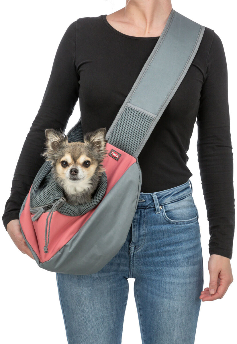 Person trägt eine rosa-graue Umhängetasche mit kleinem Hund im Inneren, schwarze Oberbekleidung, blaue Jeans.