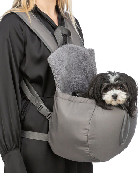 Eine Person trägt einen grauen Haustiertragerucksack mit einem kleinen Hund darin, die Tasche hat eine weiche Fütterung.