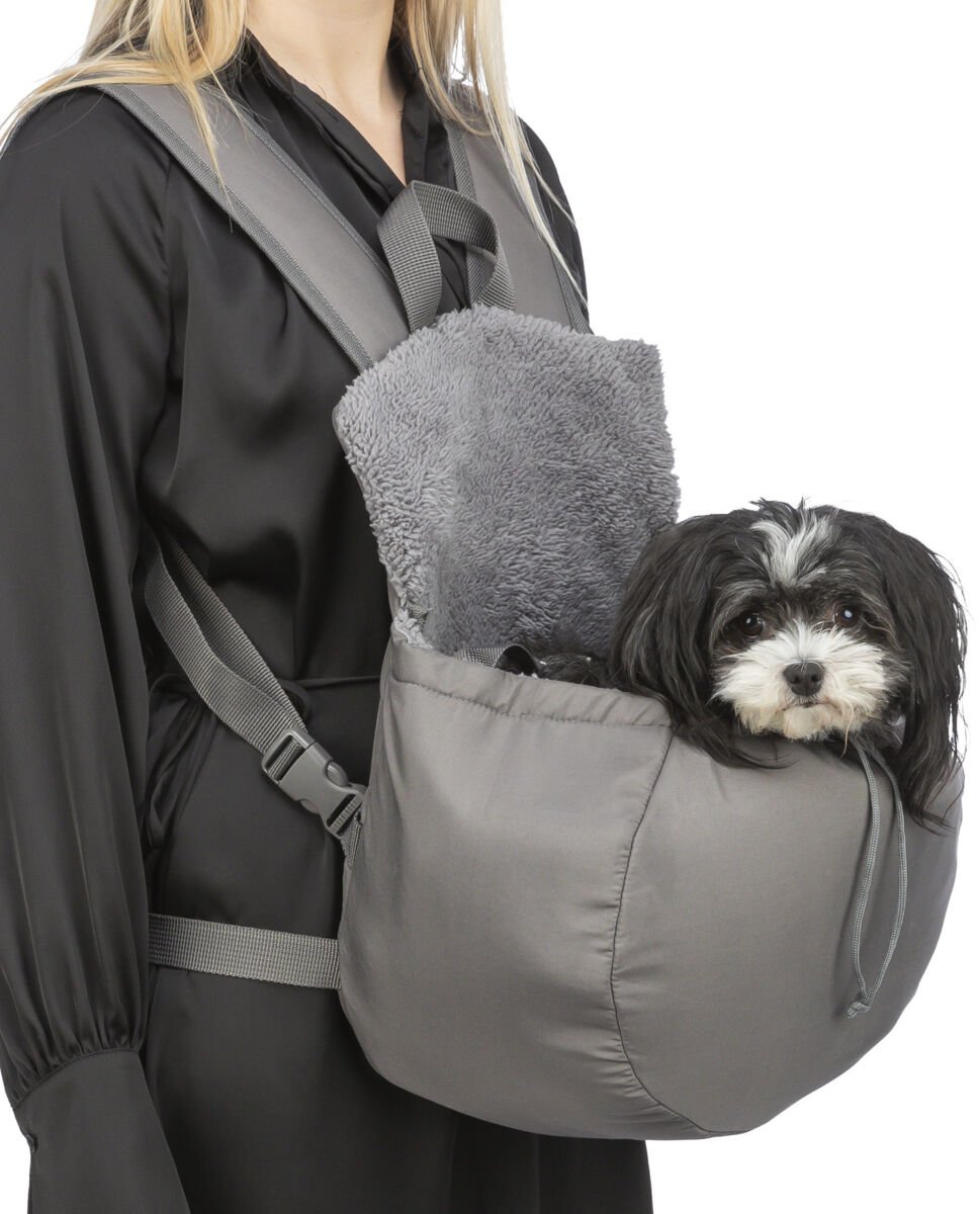 Eine Person trägt einen grauen Haustiertragerucksack mit einem kleinen Hund darin, die Tasche hat eine weiche Fütterung.
