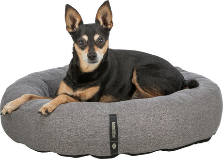 Ein kleiner Hund liegt in einem grauen, runden Hundebett mit einem Label "homedition".