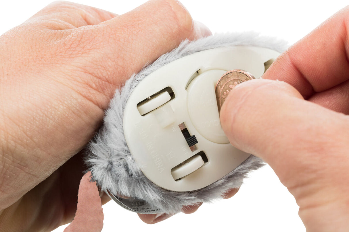 Hände halten ein kleines, weiches, graues Gerät, mit einer Münze wird ein Fach an der Unterseite geöffnet.