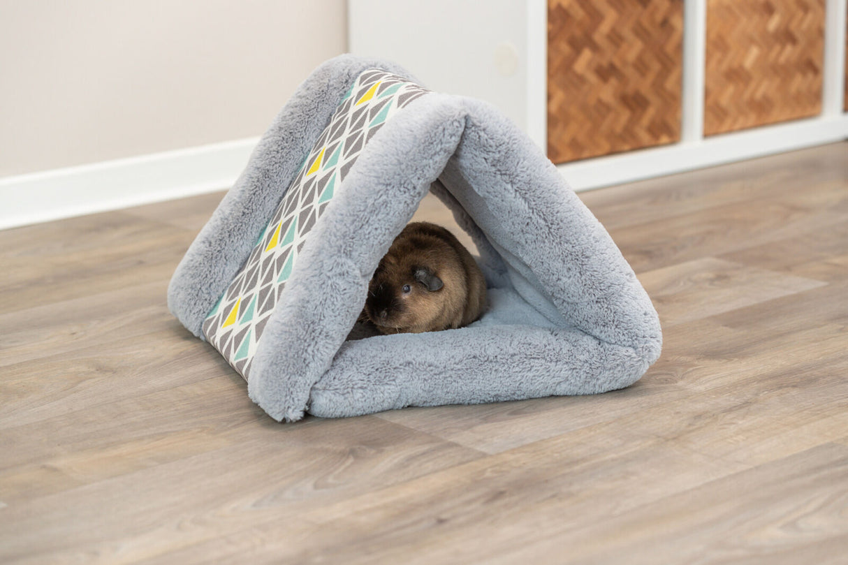 Graues, dreieckiges Plüschhaus mit geometrischem Muster auf einem Holzboden, ein kleines Tier sitzt darin.