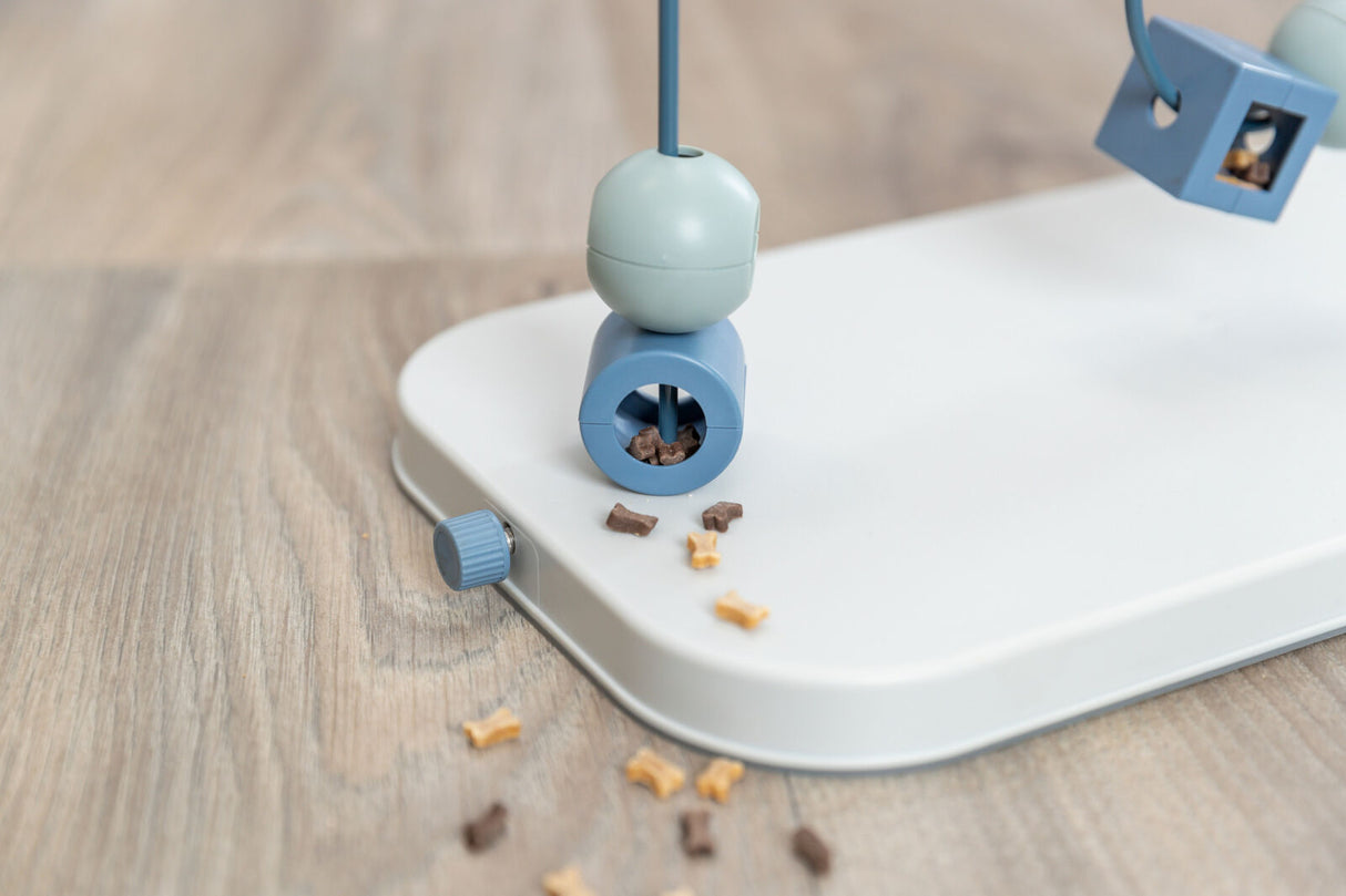 Blaues Spielzeug mit runden und eckigen Elementen auf weißer Platte, verstreute kleine Kekse, Holzhintergrund.