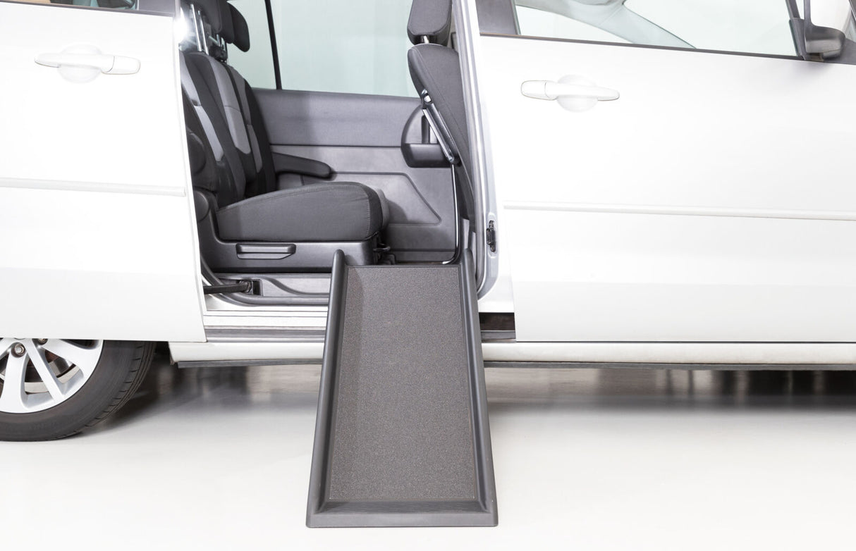 Silbernes Auto mit geöffneter Tür, schwarze Rampe führt von der Bordsteinkante zum Innenraum.