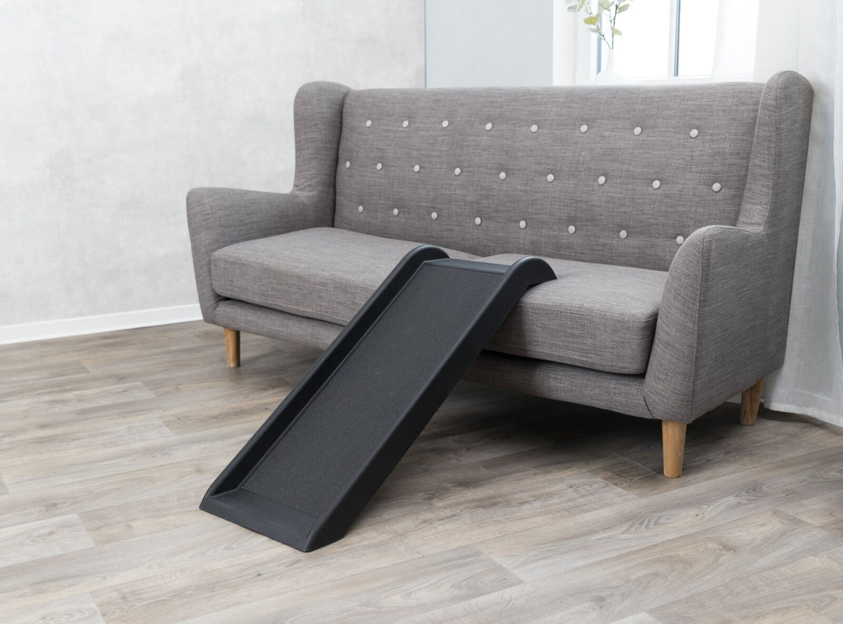 Graues Sofa mit Holzbeinen und gepolsterter Rückenlehne, davor eine schwarze Rampe auf hellem Holzboden.