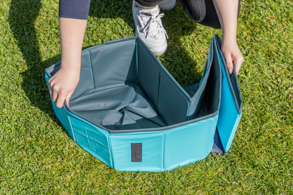 Eine Person stellt ein faltbares blaues Behältnis auf einer Grasfläche auf.
