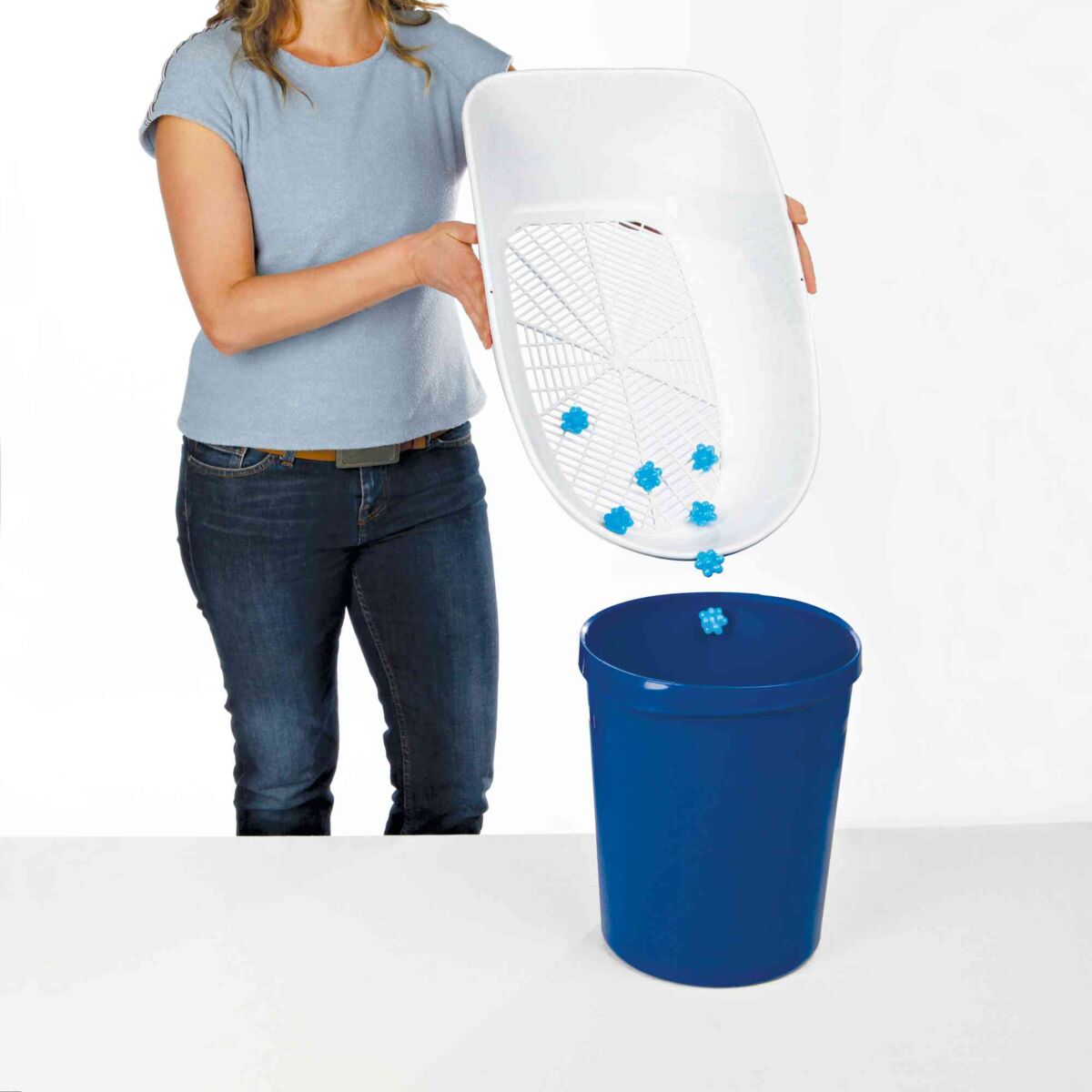 Eine Person mit graublauem Shirt hält ein weißes Sieb und lässt blaue Gegenstände in einen blauen Eimer fallen.
