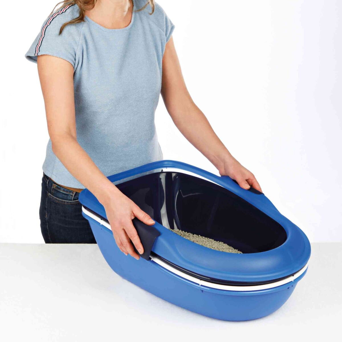 Eine Person in einem blauen Shirt hält eine ovale, blaue Katzentoilette ohne Haube auf einem weißen Untergrund.