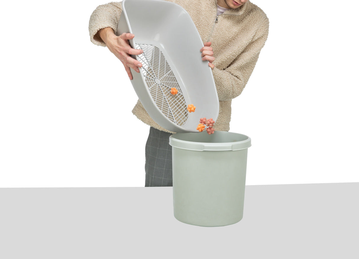 Person leert weißen Behälter mit Gittereinsatz in grauen Eimer, orange Klumpen fallen heraus.