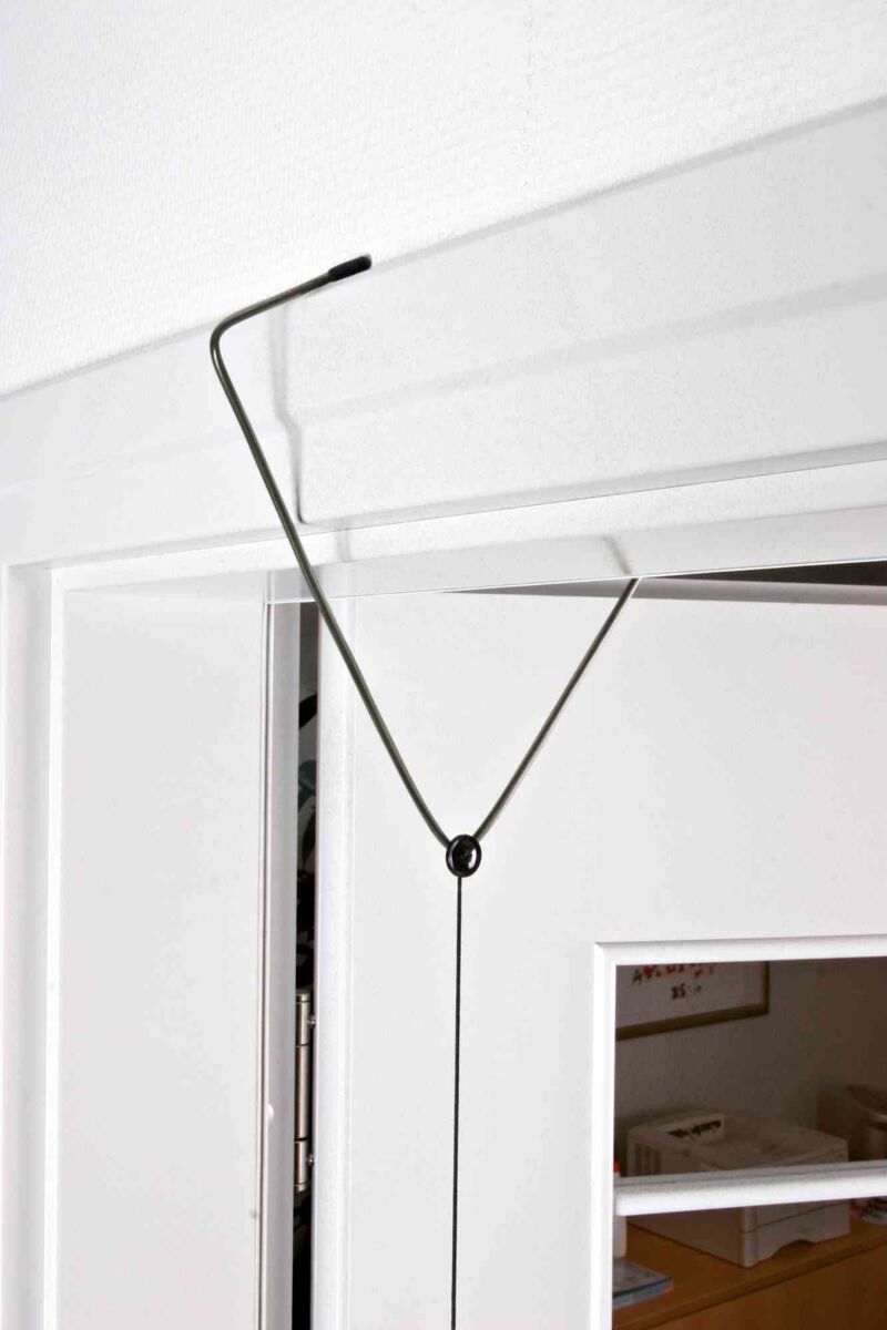 Ein Metallhaken mit schwarzem Seil ist an einer Tür befestigt, die einen Spalt offen steht.