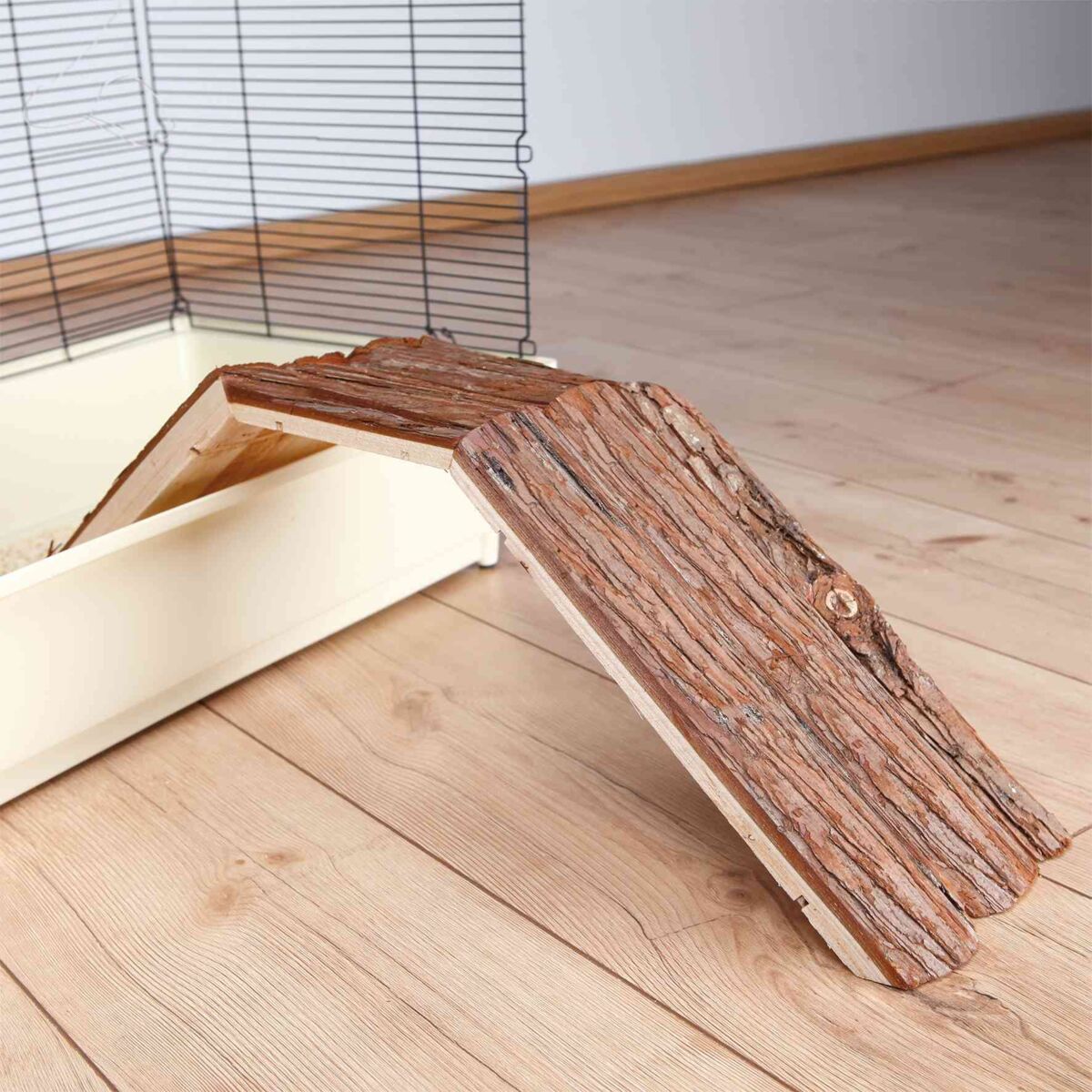 Holzrampe mit Struktur auf hellem Holzboden neben einem Gitterkäfig mit beige Bodenwanne.