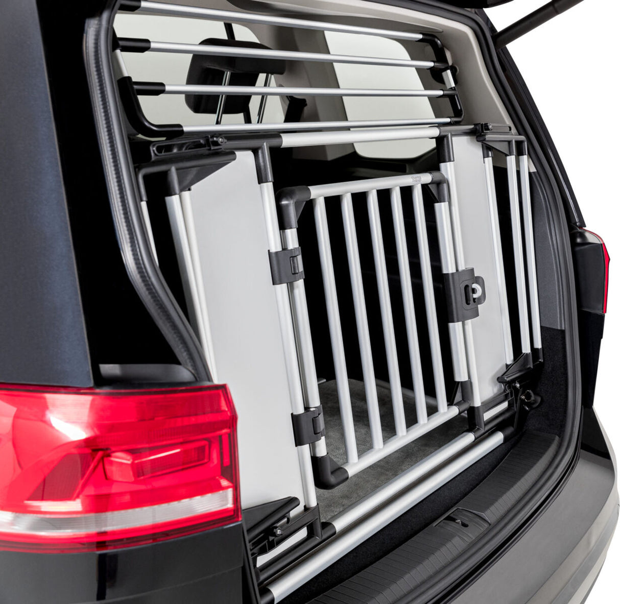 Transportbox aus silbernem Metall mit Gitter in einem geöffneten Kofferraum eines schwarzen Fahrzeugs.