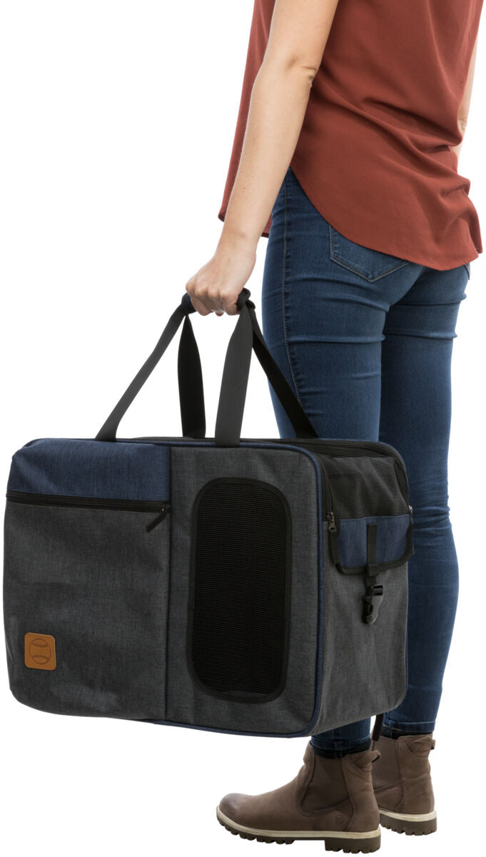 Eine Person in blauer Jeans hält eine große schwarze Tragetasche mit Netzwand und Taschen, steht auf hellem Hintergrund.