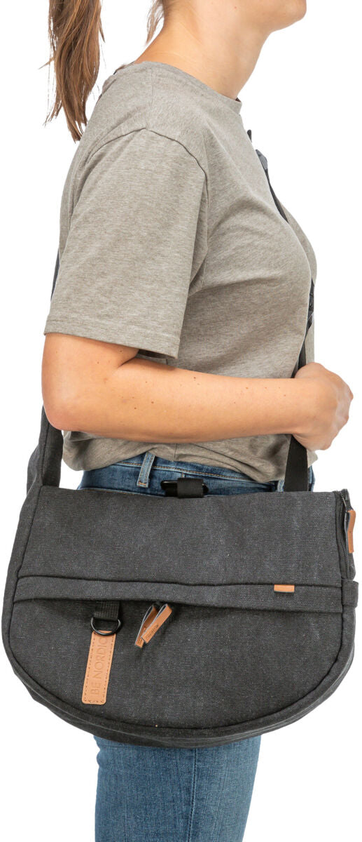 Person in grauem T-Shirt und Jeans trägt eine dunkelgraue Umhängetasche mit Lederdetails.