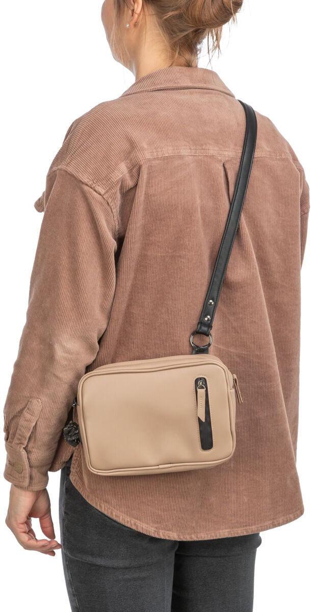 Eine Person in einem beigefarbenen Hemd trägt eine beigefarbene Tasche mit schwarzem Riemen über der Schulter.