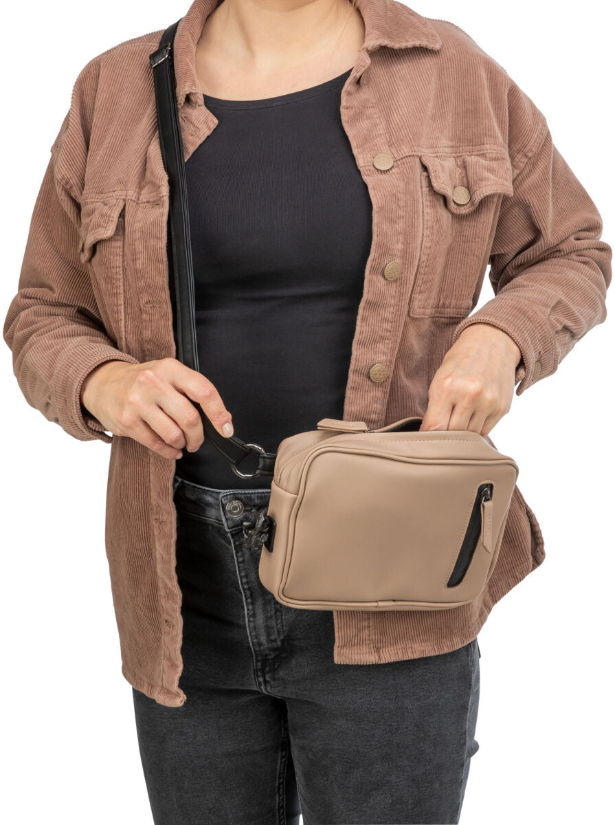 Person trägt eine beige Umhängetasche mit schwarzem Riemen, bekleidet mit brauner Jacke und schwarzem Oberteil.