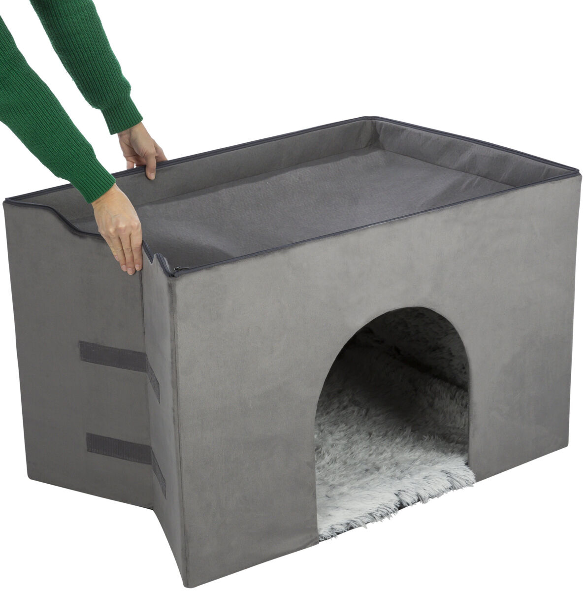 Grauer, rechteckiger Höhlenwürfel mit gewölbtem Eingang und weicher, heller Innenfläche, Person hält ihn oben.