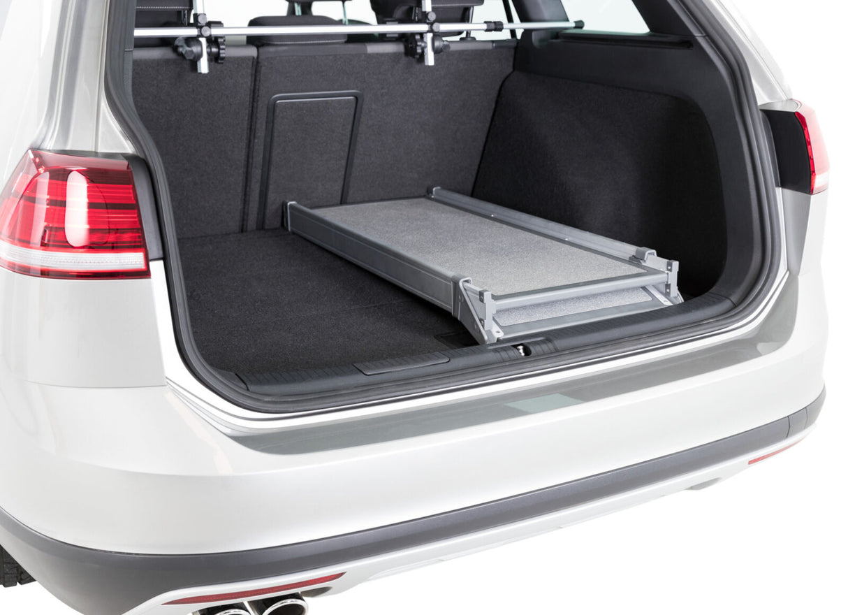 Der geöffnete Kofferraum eines weißen Autos mit schwarzem Innenraum und einer ausgeklappten Metallrampe.