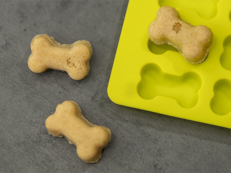 Selbstgebackene Hundekekse in Knochenform auf gelber Backmatte
