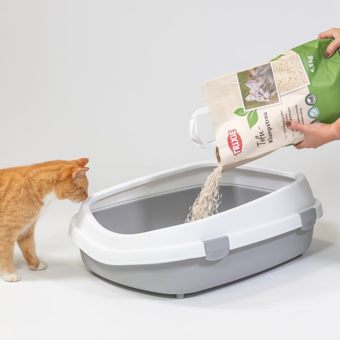 Rote Katze vor Katzentoilette die dabei zuschaut wie das Katzenklo mit Tofu Streu befüllt wird