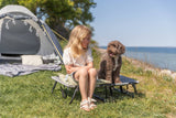 Mädchen sitzt neben einem braunen Hund vor einem Zelt am Seeufer.
