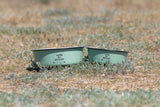 Zwei grüne Schüsseln auf Gras mit Aufschrift "ready for adventure", im Hintergrund verschwommene Wiese.