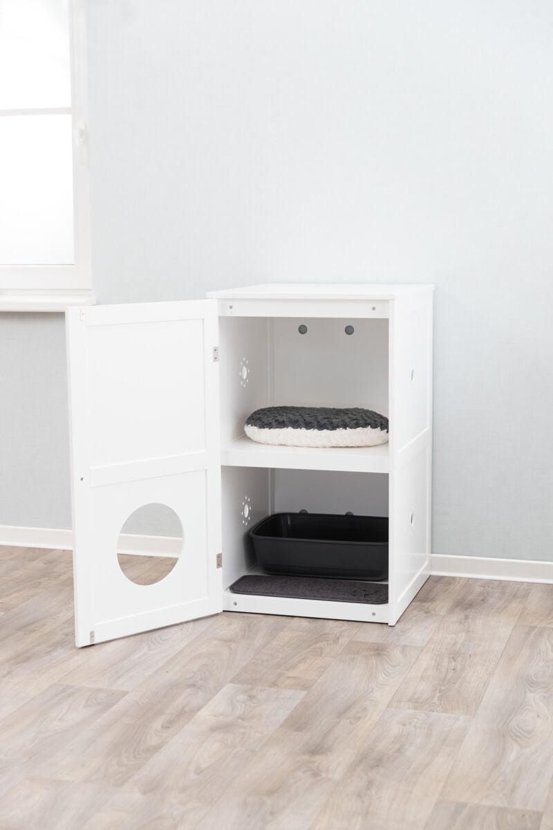 Ein weißes Schrankmöbel mit offener Tür zeigt eine schwarze Katzentoilette unten und ein rundes Kissen oben.